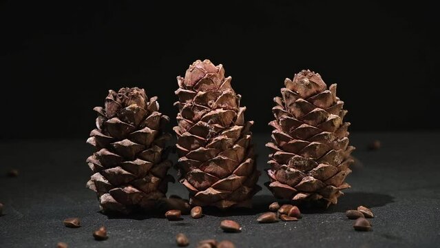 Pine nuts fall into a wooden bowl on a black background. Superfood pine nuts. Cedar cones.