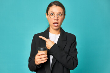 A young caucasian business woman holds a takeaway coffee pointing to the side