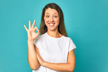 Fototapeta premium A young caucasian woman isolated winks an eye and holds an okay gesture with hand.