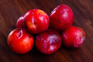 Fototapeta na wymiar Closeup of ripe red plums on wooden background. Organic fruits concept