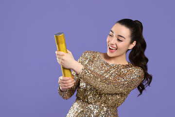Young woman blowing up party popper on purple background, space for text