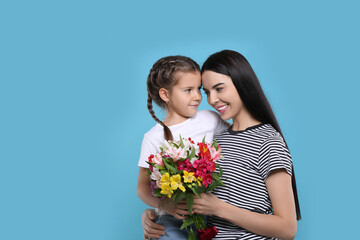 Happy woman with her daughter and bouquet of beautiful flowers on light blue background, space for text. Mother's day celebration