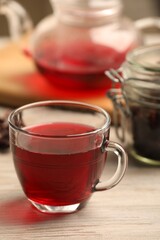 Cup of delicious hibiscus tea on white wooden table, closeup