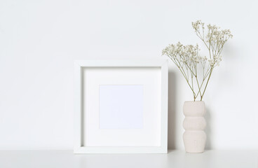 Empty photo frame and vase with dry decorative gypsophila flowers on white table. Mockup for design