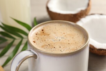 Cup of coffee, halves of coconut and green leaves on table, closeup