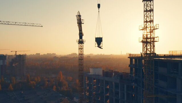 Aerial side view of a tower cranes silhouettes at the construction site of a residential building