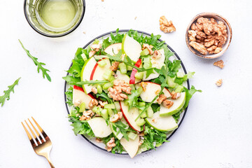 Waldorf salad with red and green apple, green celery, lettuce, arugula and walnuts on plate, white table background, top view