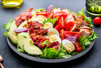 Cobb salad with chicken fillet, tomatoes, eggs, bacon, avocado and lettuce, dark table background,...