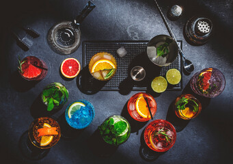 Cocktails set on black bar counter, top view. Mixology concept. Assortment of colorful strong and low alcohol drinks for cocktail party. Dark background, bar tools, hard light