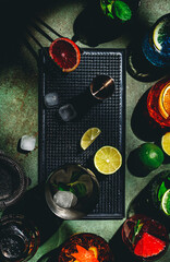 Cocktails set on rusty green bar counter, top view. Mixology concept. Assortment of colorful strong and low alcohol drinks for summer cocktail party. Dark background, bar tools, hard light