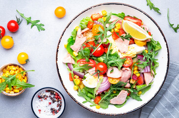 Canned tuna salad with cherry tomatoes, red onion, eggs, sweet corn, paprika, lettuce, radicchio and arugula. Gray table background, top view