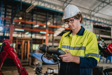Professional engineer holding robot controller checking and repairing automatic robotic machine at...