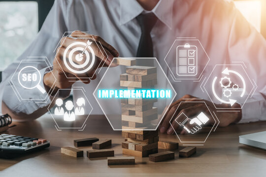 Implementation concept, Person hand piling up and stacking a wooden block with implementation icon on virtual screen.