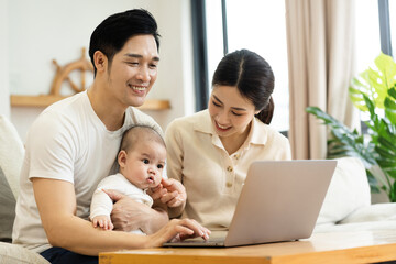 image of asian family with baby sitting on sofa using laptop