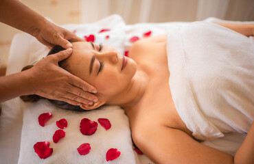 Obraz na płótnie Canvas The expert masseuse gently kneaded the scalp of the beautiful asian customer with both hands on a bed strewn with rose petals.