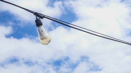 Hanging lightbulbs connected by a cable with a blue sky background. Close-up light chain decoration with blue sky background. festive lights garland. light bulbs on string wire. Daylight.