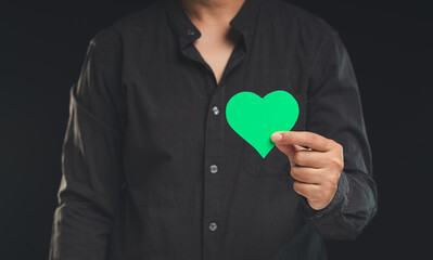 Environmental and ecology care concept. Hand holding a green heart shape symbol while standing against a black background