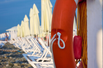 Deserted beach by the sea with smooth rows of white sun loungers with umbrellas. Lifebuoy hangs on...