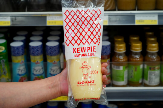 Tokyo, Japan - April 15, 2023 : Close up of Japanese style Kewpie brand mayonnaise held in hand in a local supermarket aisle with labels and prices visible in the background.