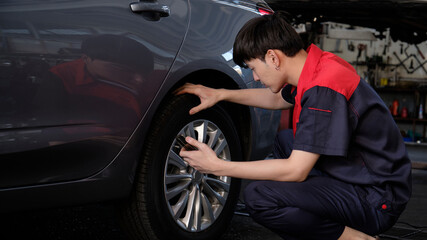 Plakat Young male Asian professional automotive mechanical worker checks tire pressure by smartphone application at a car garage, expert in maintenance vehicle service, and fixing occupations auto industry.