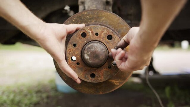 Close-up point of view of caucasian male removing rusty brake disc from car axle