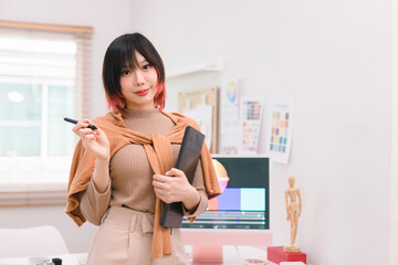 A portrait of a beautiful, professional, and confident millennial creative and stylish young female freelance designer hands holding a tablet and stylus pen while standing at her desk in office.