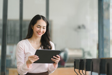 A portrait of a smiling, young, beautiful, professional, and confident millennial Asian businesswoman using a digital tablet to analyze sales data at a co-working space.