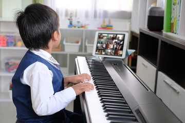 Young pianist boy looking at the digital tablet screen for learning piano online at home. Music...