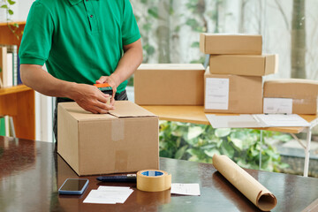 Mail worker sealing cardboard boxes before shipping goods to customer - obrazy, fototapety, plakaty