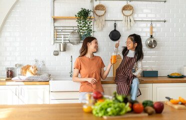 Portrait of enjoy happy love asian family mother with little asian girl preparing drinking glass of fresh juice and orange on counter in kitchen at home.Diet concept.healthy drink