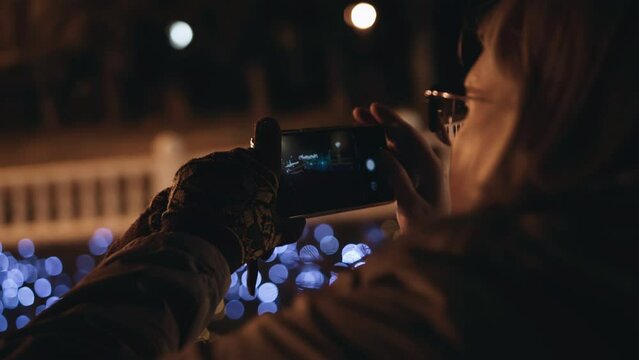 The girl shoots a cool night atmosphere of a night festive city on a mobile phone