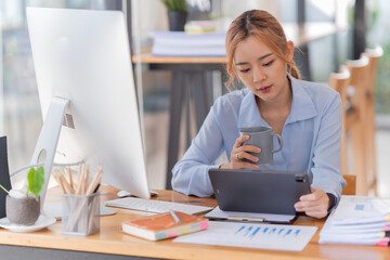 happy young businesswoman Asian siting on the chairs cheerful demeanor raise holding coffee cup smiling looking laptop screen .Making opportunities female working successful in the office.