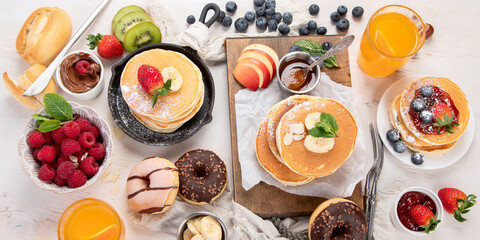 Pancakes with fresh fruits, donuts and coffee on a white background.