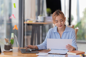 happy young businesswoman Asian siting on the chairs cheerful demeanor raise holding coffee cup smiling looking laptop screen. Making opportunities female working successful in the office.