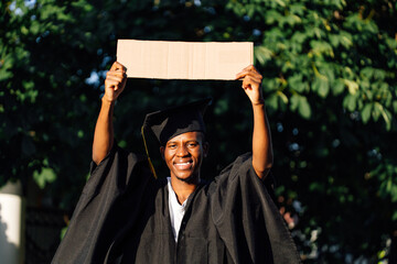 Portrait of smiling black guy standing with upraised empty cardboard poster on street looking for...