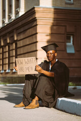 Happy black guy sitting with cardboard poster on street looking for job. University or college...