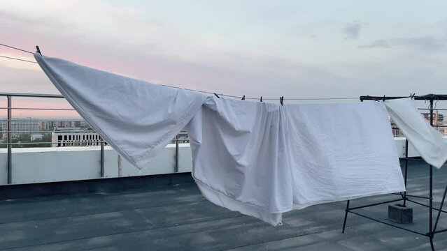 A lot of white sheets are dried in the sun rope on the roof top. Sunset. High quality 4k footage with slow motion