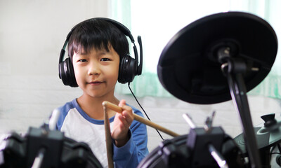 Asian child boy hold drumstick to play electronic drum with headphone and happy smiling face at...