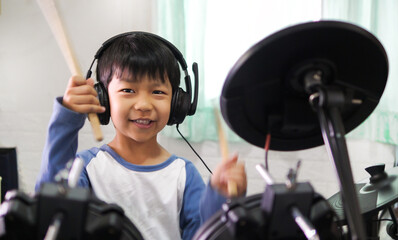 Asian child boy hold drumstick to play electronic drum with headphone and happy smiling face at...