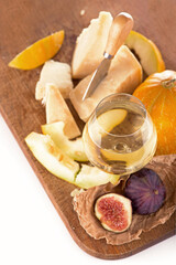 Cheese plate served with grapes, melon, figs, crackers, honey, nuts and white wine on a wooden table