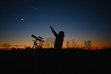 Astronomer looking at the starry skies and crescent Moon with a telescope.