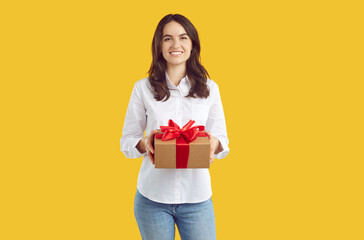 Happy brunette woman office worker in white shirt and jeans is holding a present gift in hands on yellow background. Craft giftbox, present with red tie. Discount, sale, advertisement banner concept.