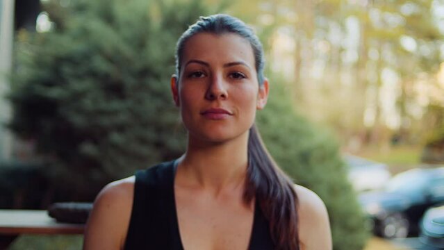 A young woman in a black tank top takes time to reflect on her golden hour workout with a ponytail and an intense stare.