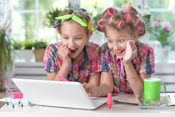 Cute twin girls in hair curlers with laptop at home