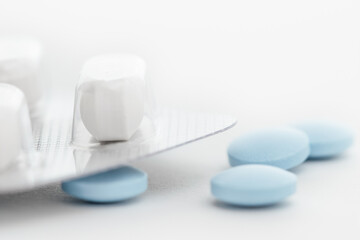 White pills in a blister and blue pills loose lying on a white table.
