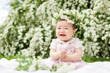 Sweet smiling little girl with wreath of spirea flowers in pink dress.