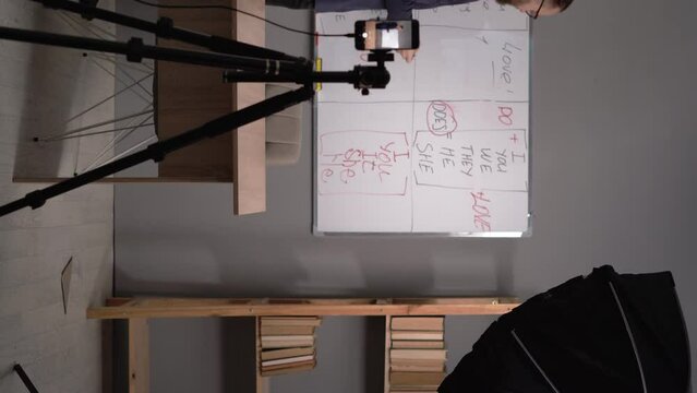 Caucasian male teacher making video lecture teaching English online standing near blackboard and livestreaming at home. E-teaching and educational blogging concept