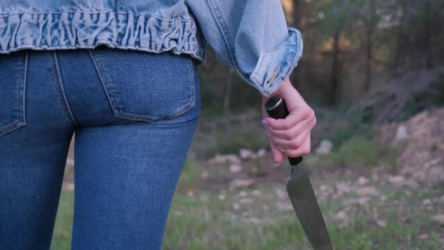 A girl in jeans with a knife in her hands walks through the forest.