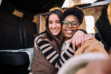 selfie photo of two happy women embracing in camper van during a road trip, concept of weekend getaway and female friendship, copy space for text
