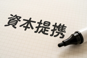 資本提携と書かれたノートとマーカー